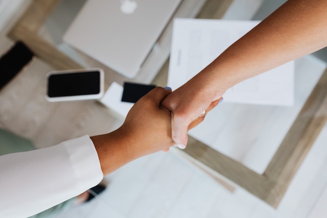 two people shaking hands across a contract on the desk between them